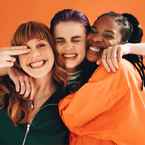 Três jovens meninas abraçadas, sorriem